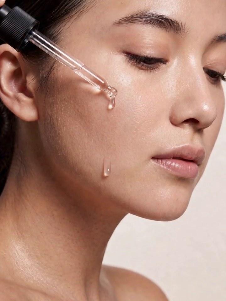 A model with dewy skin as a clear serum drop runs down her cheekbone